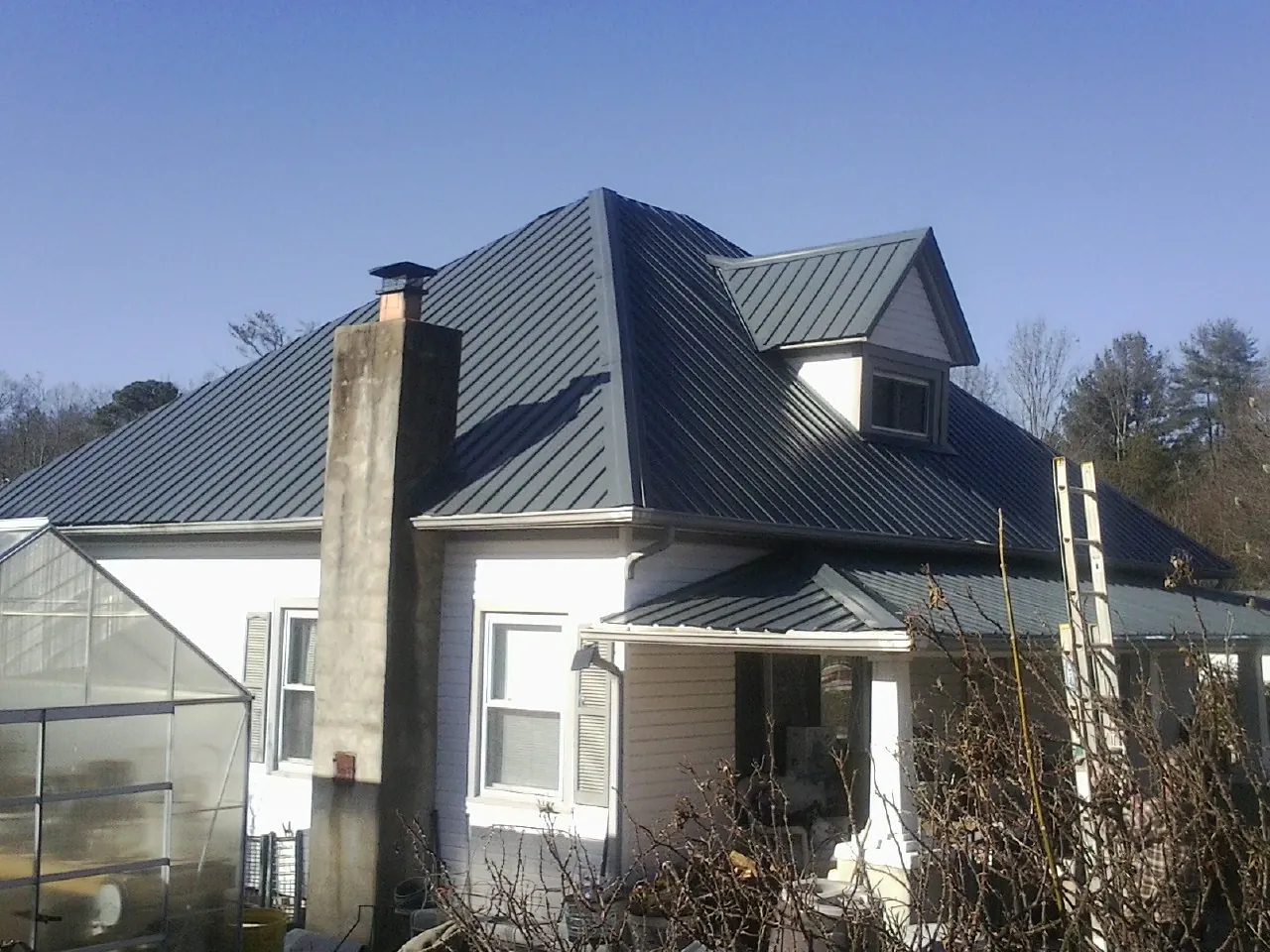 Dark blue standing seam metal roof on a white farmhouse with dormer — Slate & Tile Roof Repair by Roofing Brothers in Altoona