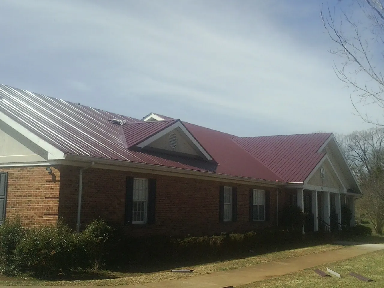 Red metal roof with gabled entries on a long brick building, from a Hail Damage Roof Repair job in Altoona
